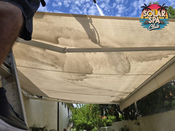 Looking up at a patio awning mid-wash, with brown runoff streaking the fabric and spray coming from above