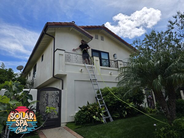 Technician on a ladder at a second-floor balcony softwashing the stucco of a two-story home
