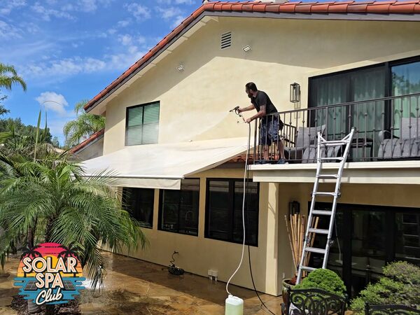 Technician softwashing the stucco wall of a two-story home from a second-floor balcony