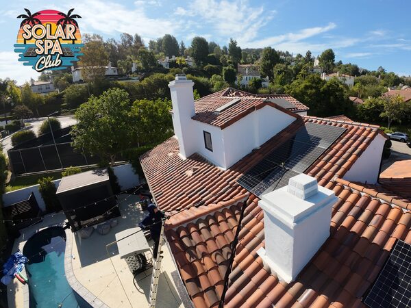 Technician on a ladder cleaning solar panels on a tile roof, seen from above
